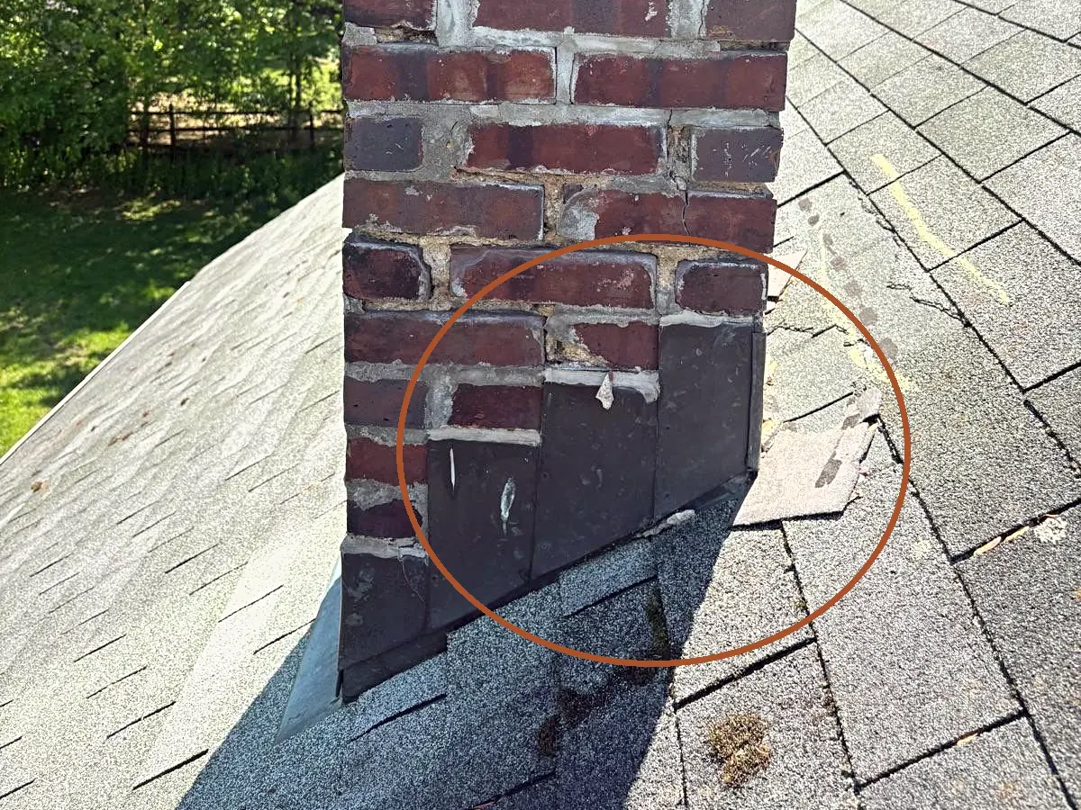 Loose step flashing and broken shingles along the side of a brick chimney, circled, from a Pujols Roof Health Report.