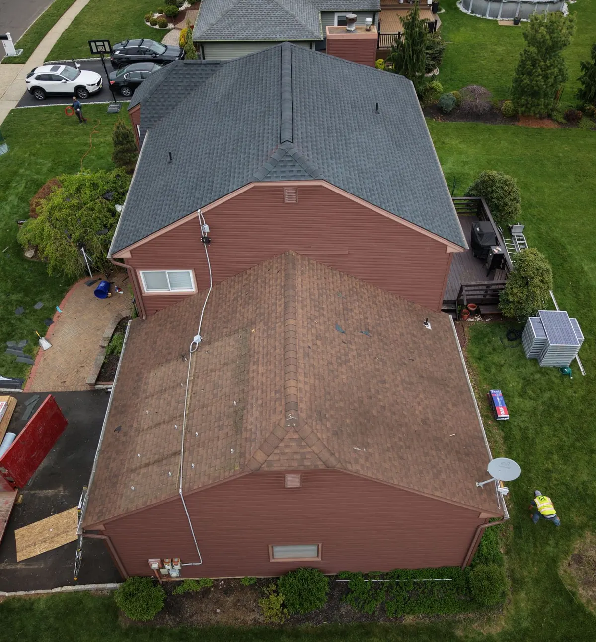 Roof replacement in progress in Hillsborough, NJ from the air: old brown shingles still on the front, new GAF Timberline HDZ in Charcoal on the back, solar panels stacked on the lawn.