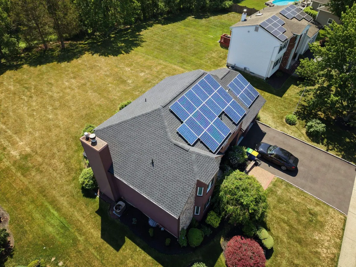 Drone view of a new GAF Timberline HDZ roof in Charcoal with the solar panels reinstalled, on a stone-front colonial in Hillsborough, NJ, roof replacement by Pujols Roofing & Siding LLC.