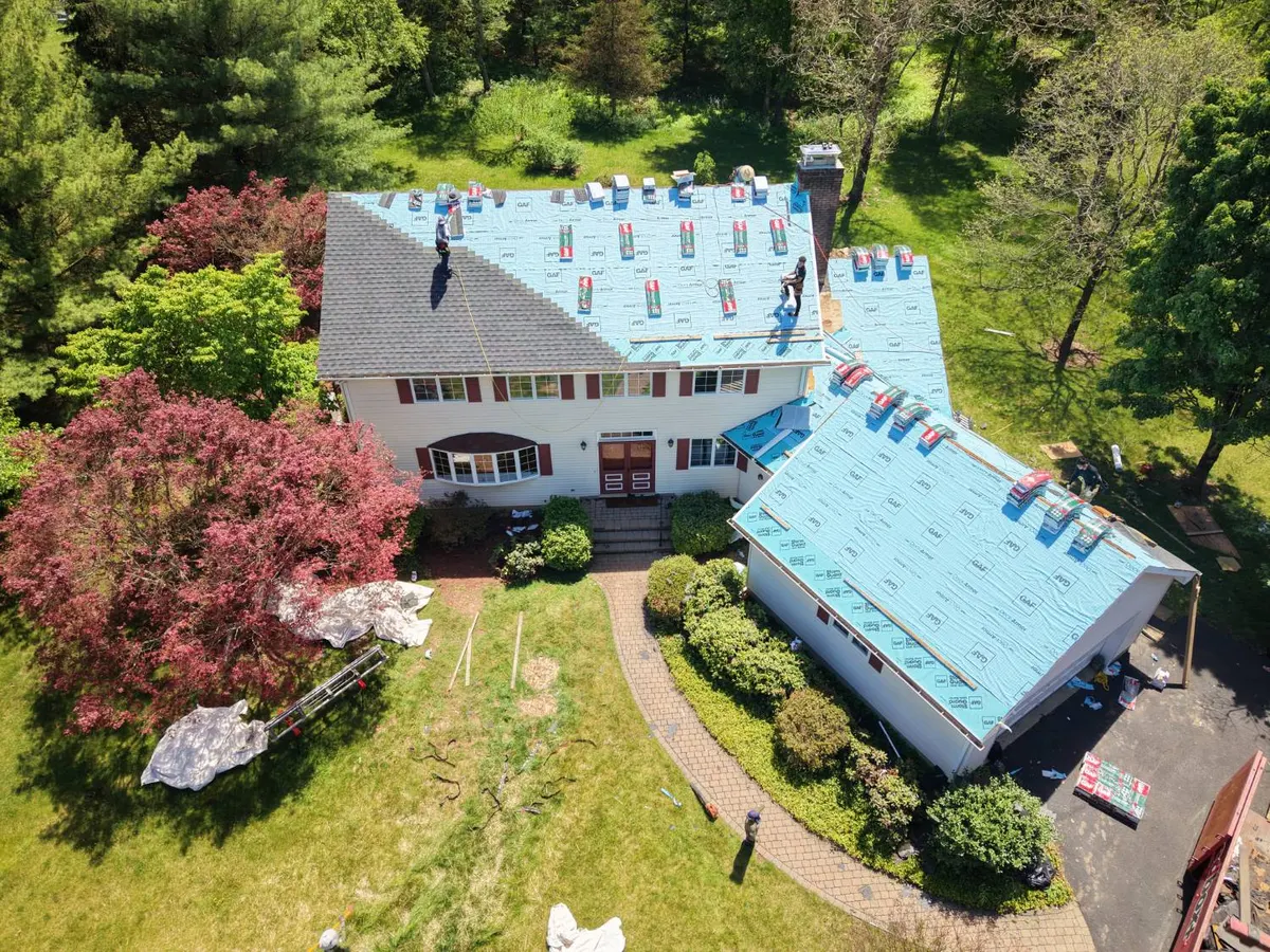 Pujols crew laying blue GAF Deck-Armor underlayment and new GAF Ultra Timberline HDZ (UHDZ) shingles in Charcoal on a white colonial in Montgomery, NJ during a two-day roof replacement.