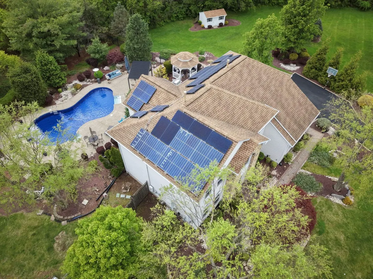 Drone view of a new GAF Timberline HDZ roof in Weathered Wood with the solar panels reinstalled after a fire, on a two-story home with a pool and gazebo in Franklin Township, NJ, by Pujols Roofing & Siding LLC.