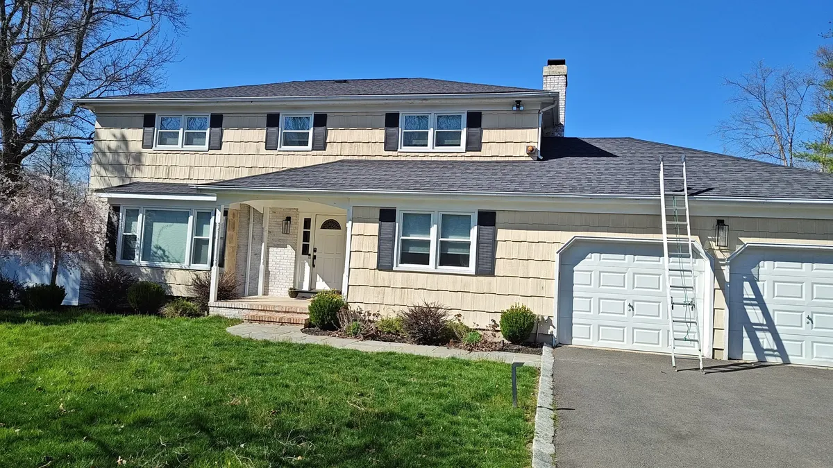 The front of a Cherry Brook Drive house in Princeton, NJ after new siding, with a ladder at the garage, by Pujols Roofing & Siding.