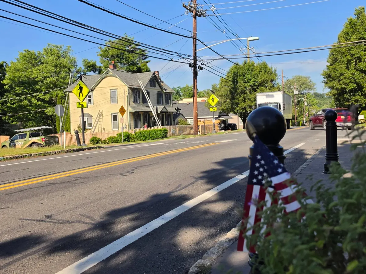 A yellow 1900 home on Washington Street in Rocky Hill, NJ with ladders on the roof during the work, seen from across the street, the Pujols truck parked out front.