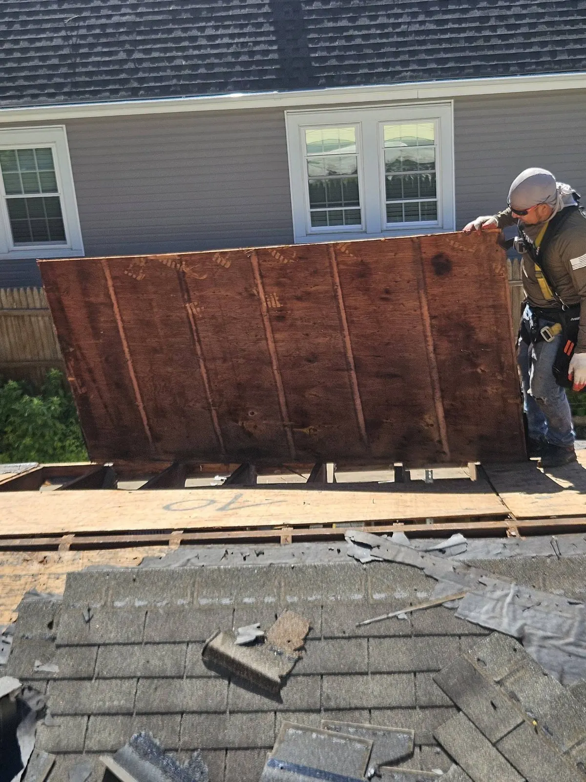 A Pujols crew member lifting a sheet of rotted roof decking off the open rafters of a Rocky Hill, NJ roof during the tear-off.