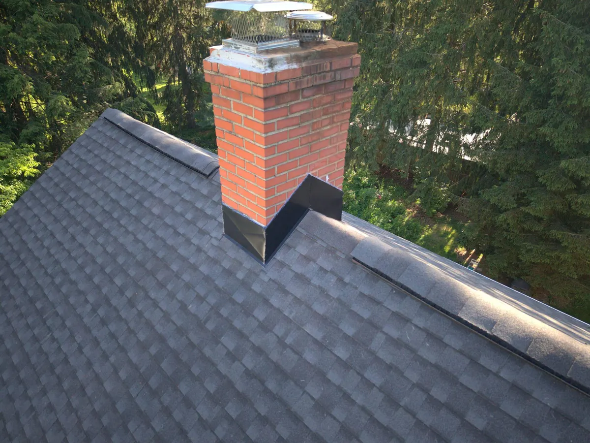 New gray shingles and fresh flashing around the brick chimney on a Rocky Hill, NJ roof by Pujols Roofing.