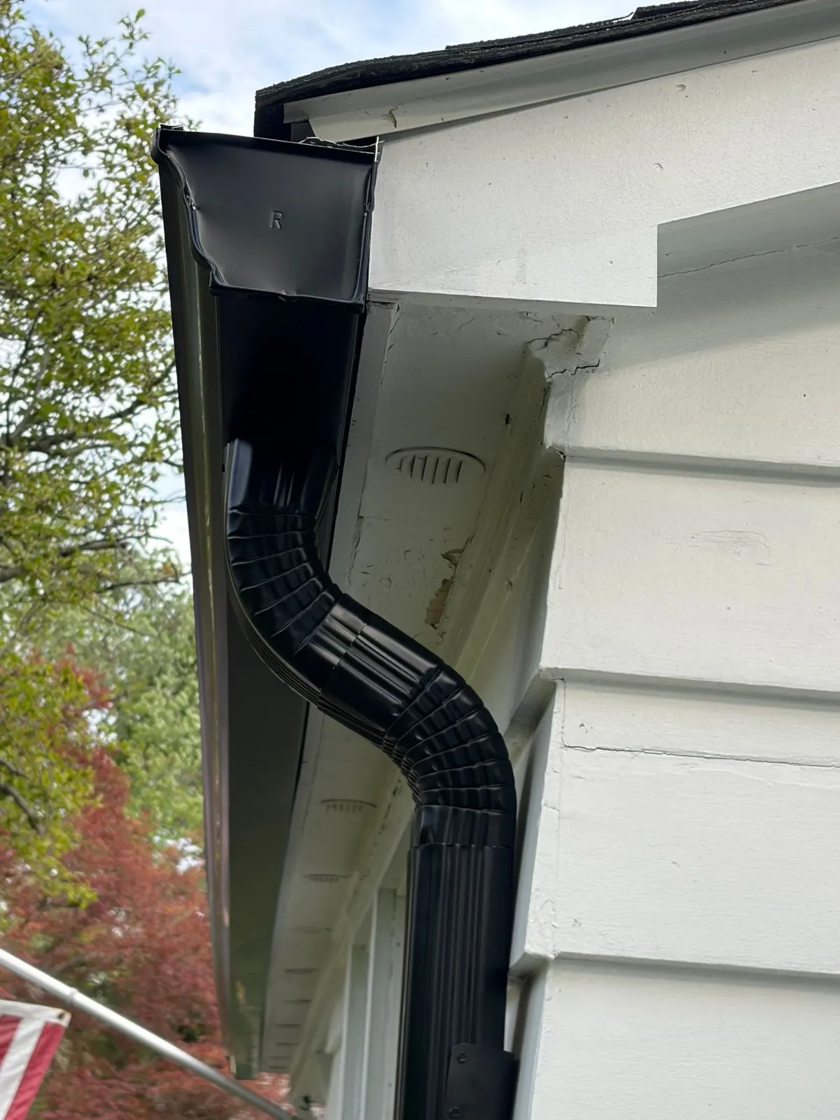 Close-up of a new black gutter corner and downspout at the eave of a white house in Rocky Hill, NJ, by Pujols Roofing.