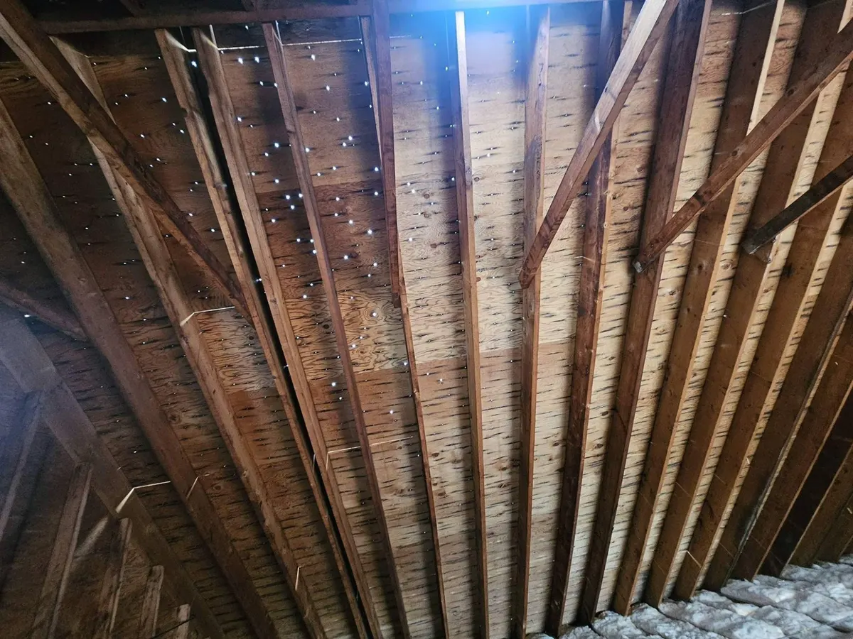 Daylight showing through nail holes in the old roof deck, seen from inside the attic of an 85-year-old home in Toms River, NJ, before the roof replacement.