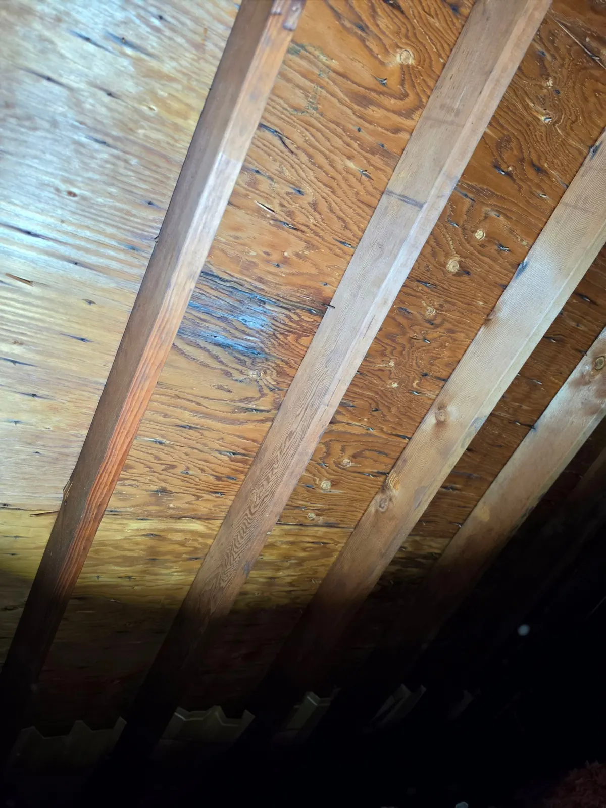 Dark, heat-stained plywood roof decking between the rafters, seen from inside the attic of a Rocky Hill house.