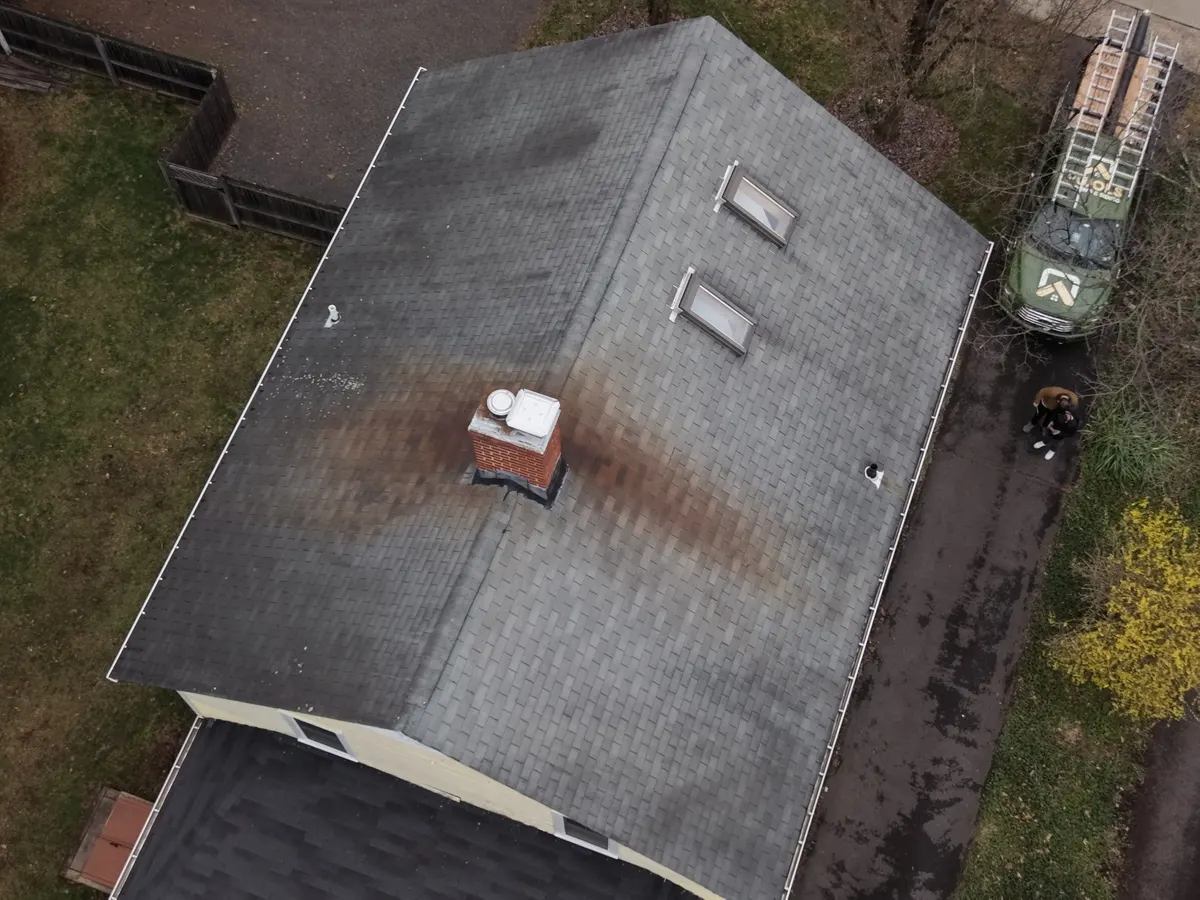 Drone view of a worn asphalt roof with a brick chimney and dark staining on a Rocky Hill home, before replacement by Pujols Roofing.