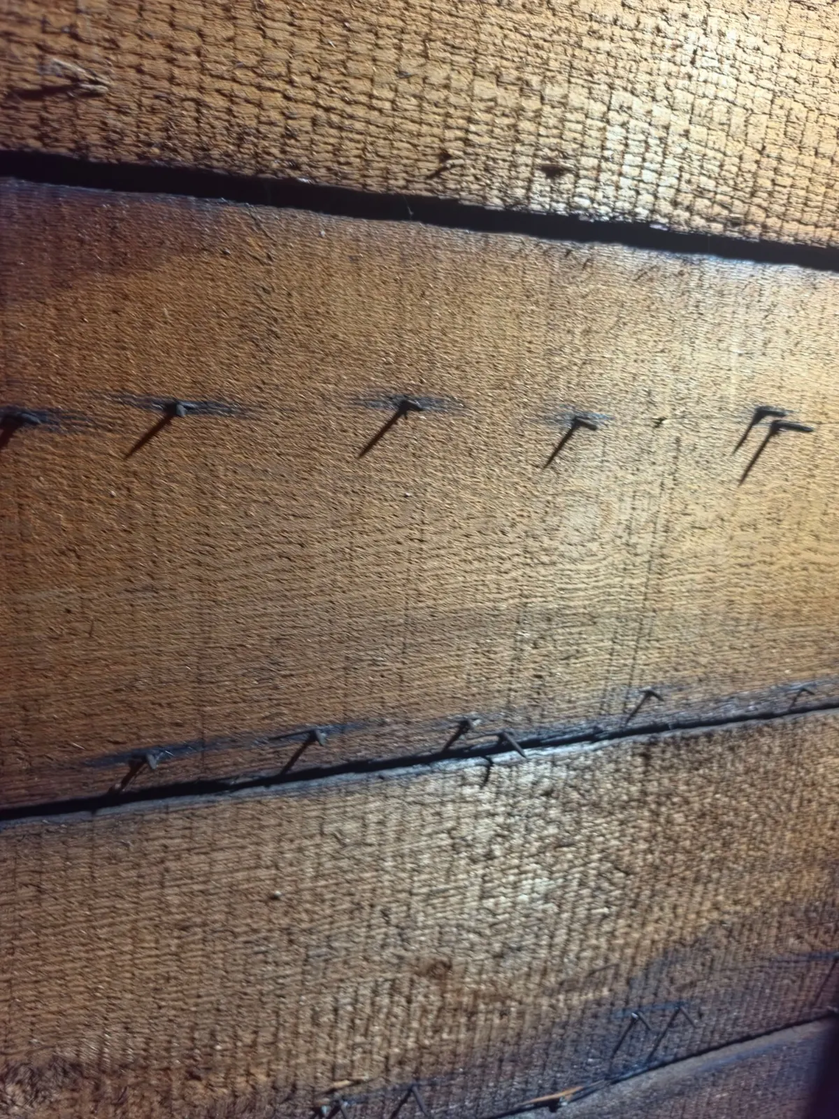 Wide wooden plank roof decking with gaps between the boards, seen up close from inside the attic of a Rocky Hill house.