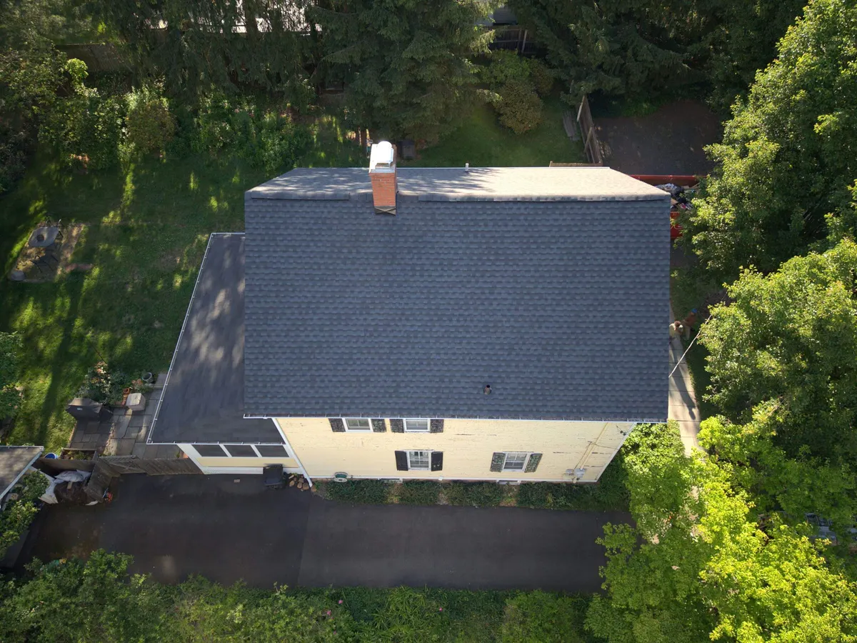 Drone view of a finished roof replacement in Rocky Hill, NJ: new dark gray shingles on a yellow two-story home, by Pujols Roofing.