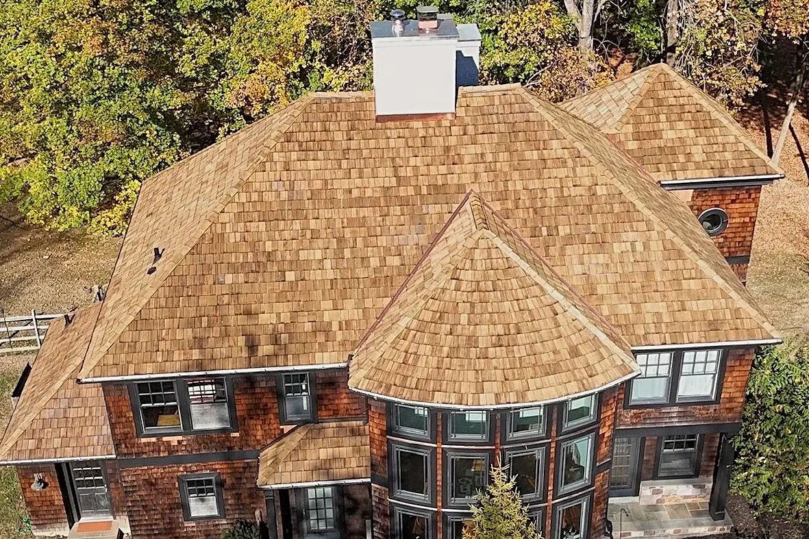 Cedar shake roof with a curved turret and copper details on a shingle-style home, a specialty roofing project.